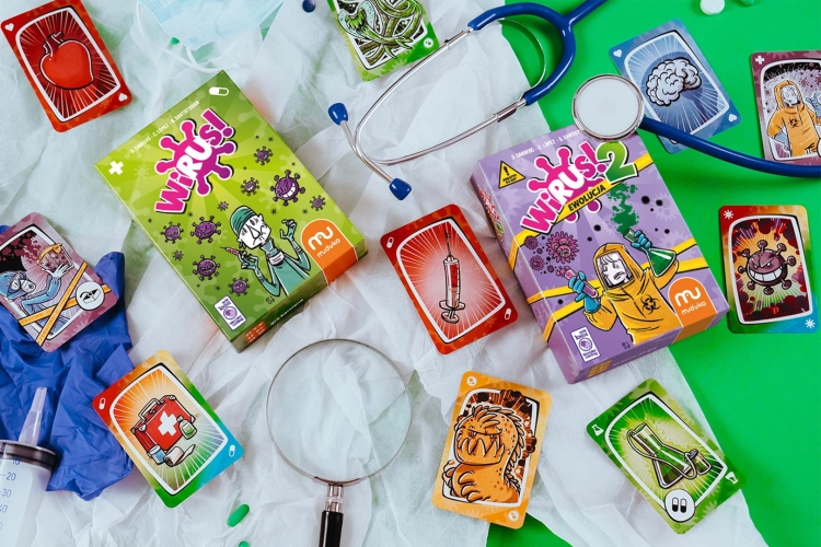 Gry „Wirus” i „Wirus 2” rozłożone na zielonym tle obok stetoskopu, lupy i rękawiczek medycznych w kreatywnej aranżacji.