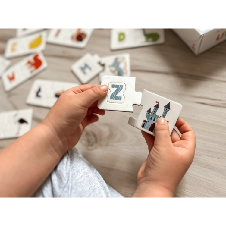 Zbliżenie na dłonie dziecka łączącego element z literą „Z” z ilustracją zamku, prezentujące mechanizm łączenia puzzli.
