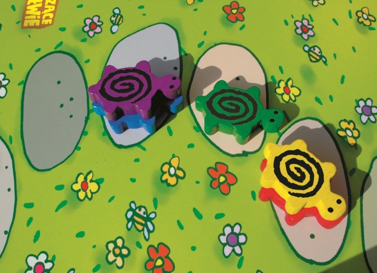 Kolorowe drewniane figurki żółwi na polach planszy; fioletowy żółw wchodzi na niebieskiego, zielony i żółty żółw stoją oddzielnie.