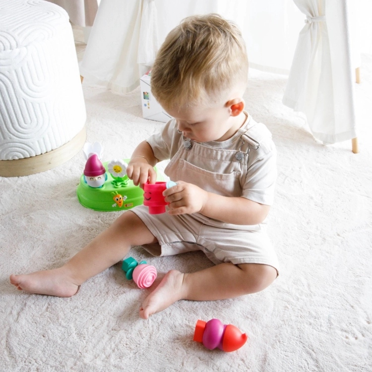 Dziecko w jasnym ubranku siedzi na podłodze i bawi się różową figurką konewki z zestawu edukacyjnego.