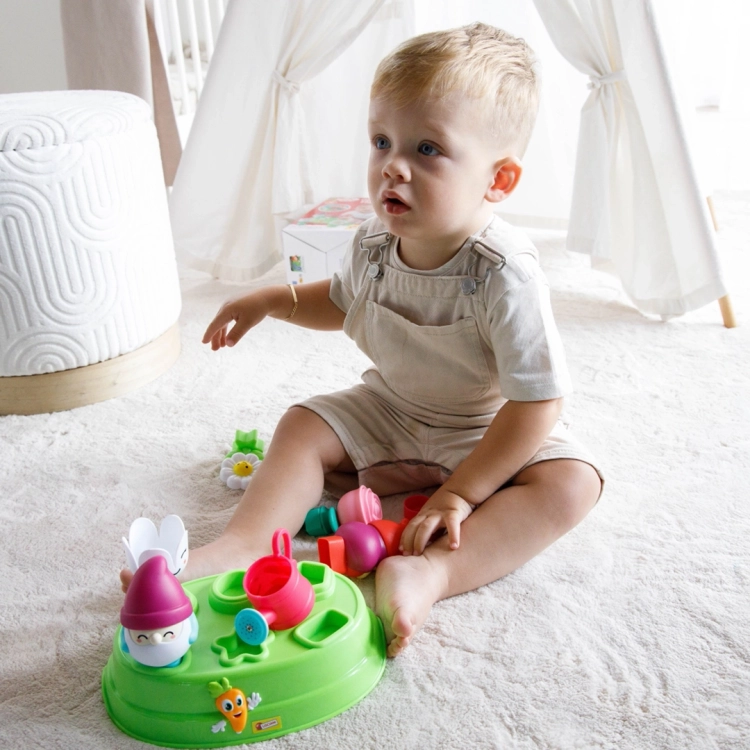 Małe dziecko siedzące na dywanie obok ułożonego sortera z krasnalami i kwiatami w pokoju dziecięcym.