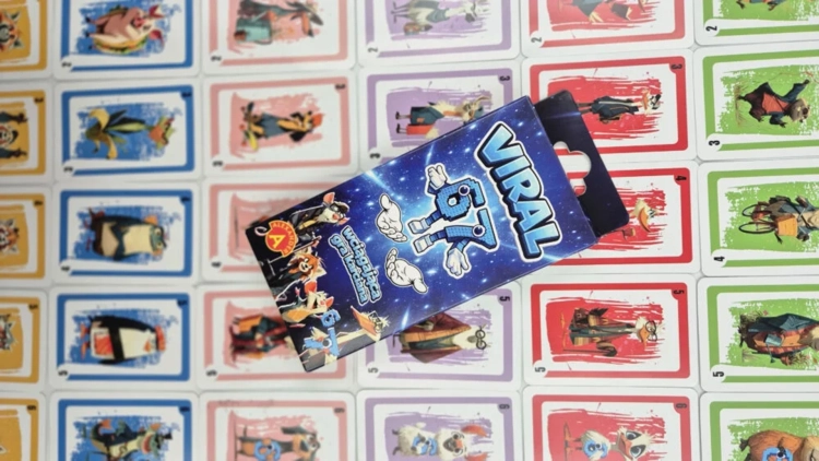 Pudełko gry „Viral 67” położone na dużej liczbie rozłożonych kart. Każda karta prezentuje unikalną ilustrację zwierzęcia na kolorowym tle z numerem w rogu.