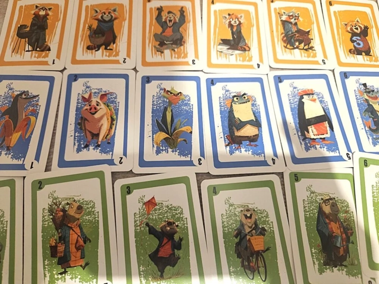Trzy rzędy kart do gry ułożone obok siebie. Górny rząd to pomarańczowe karty z pandą małą, środkowy to niebieskie z różnymi zwierzętami, a dolny to zielone karty z bobrami.