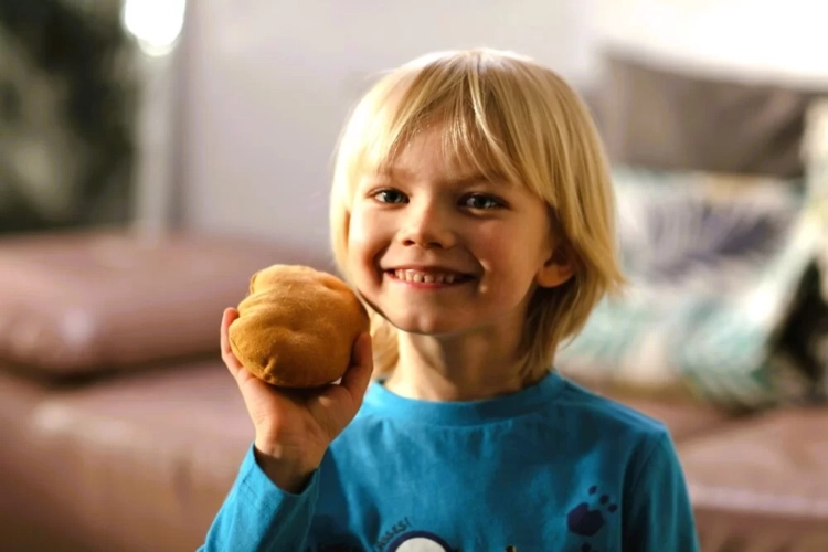 Uśmiechnięty chłopiec trzyma w dłoni pluszowego ziemniaka z gry Gorący Ziemniak.