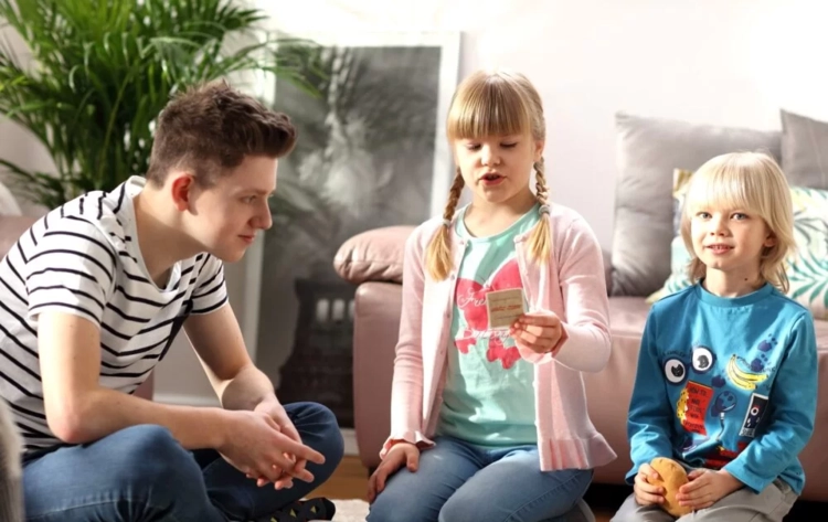 Grupa dzieci siedzi na dywanie, jedna dziewczynka czyta pytanie z karty podczas gry.