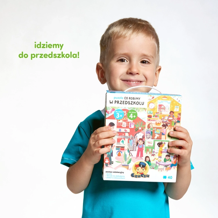 Uśmiechnięty chłopiec w niebieskiej koszulce trzyma pudełko puzzli CzuCzu „Co robimy w przedszkolu”.