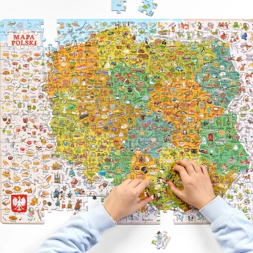 Bliskie ujęcie dłoni dziecka układającego kolorowe puzzle CzuCzu z mapą Polski, przedstawiającą liczne ilustracje zabytków i potraw.