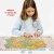 Dziewczynka w błękitnej bluzie pochylona nad niemal ułożonymi puzzlami Mapa Polski, wskazująca palcem na detale ilustracji.