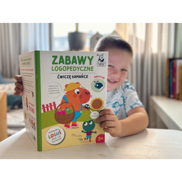 Chłopiec trzyma książkę Zabawy logopedyczne Kapibara Loguś Ćwiczę łamańce Kapitan Nauka.