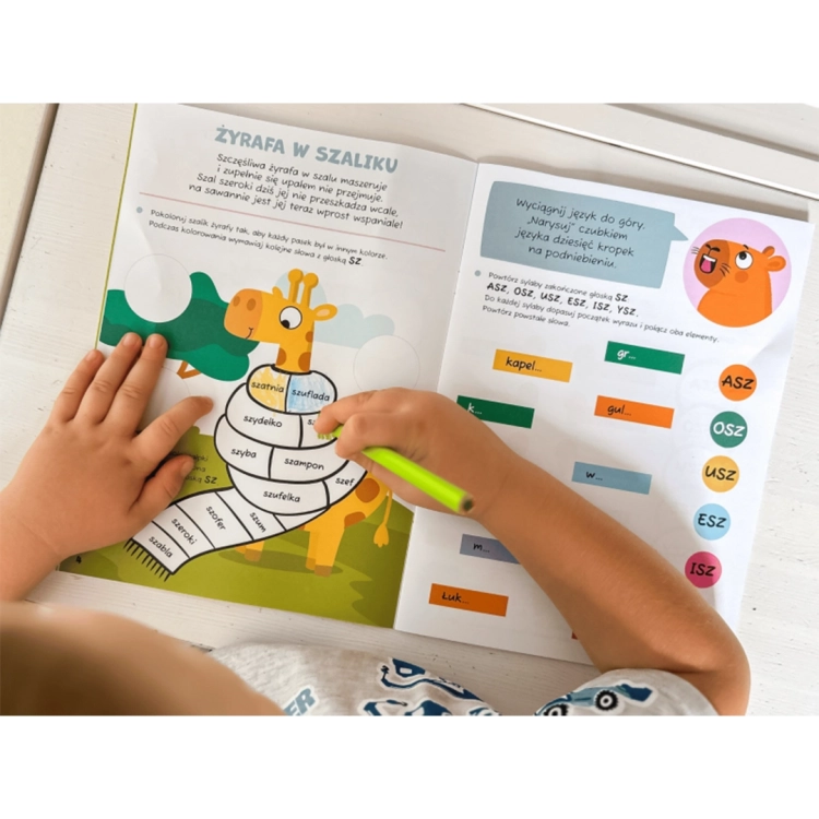 Ręce dziecka kolorujące żyrafę w szaliku w książce edukacyjnej Ćwiczę łamańce.