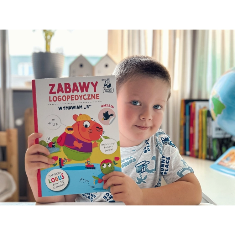 Chłopiec trzyma książkę Zabawy logopedyczne Kapibara Loguś Wymawiam R wydawnictwa Kapitan Nauka.