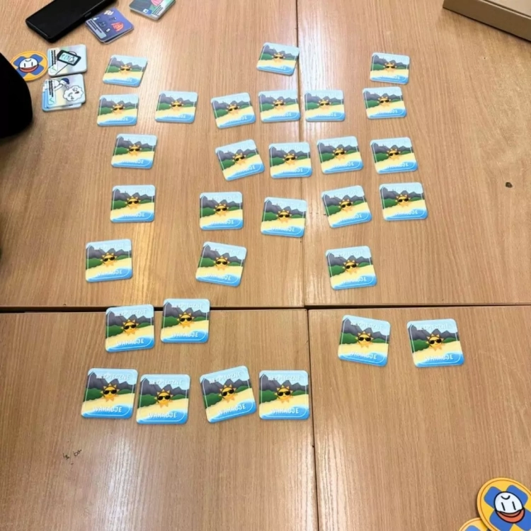 Rozłożone elementy gry Bezpieczne wakacje marki beGame na drewnianym blacie, kafelki z grafikami.