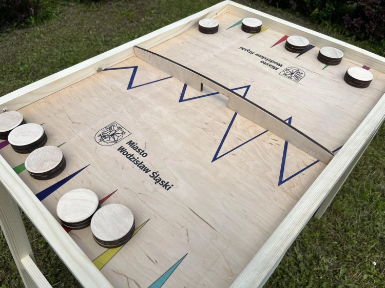 Zbliżenie na drewnianą planszę gry Hokej na gumce XXL marki Grandabox z logo Miasta Wodzisław Śląski i krążkami.