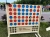 Drewniana gra "Kółko i krzyżyk na cztery" (Connect Four) w wersji XXL ustawiona w parku. Na planszy znajdują się niebieskie i czerwone krążki, a na dole widnieje napis "Miasto Wodzisław Śląski".