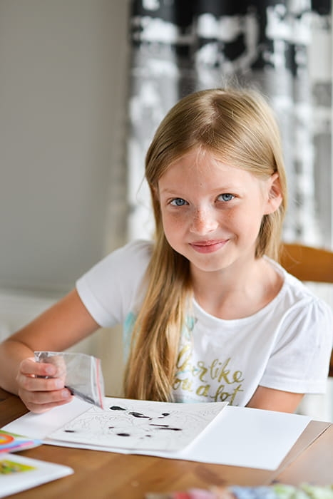 Dziecko tworzy obrazek syrenki przy użyciu piaskowych malowanek.